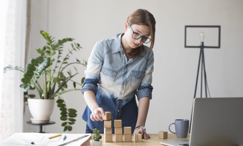 young-woman-stacking-wooden-block-work-desk-office